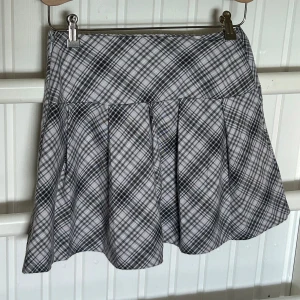 Strl 34 kort kjol med veck - Supersnygg grå och rosa rutig kortkjol med veckad design. Kjolen har en klassisk skoluniform-vibe och är perfekt för dig som gillar preppy stil. Bekväm midja och lätt utsvängd form. Passar till både sneakers och boots.