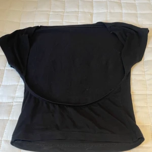 Svart croppad topp med kort ärm och öppen rygg  - En svart croppad topp med korta ärmar och öppen rygg. Perfekt för att matcha med höga jeans eller kjol. Toppens material känns mjukt och stretchigt, vilket gör den bekväm att bära hela dagen.