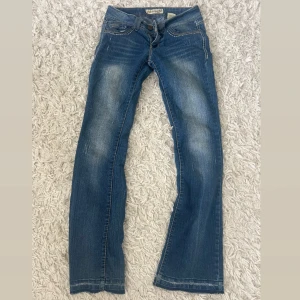 Bootcut jeans från Paris Blues - Blå bootcut jeans från Paris Blues med låg midja och snygga slitningar. Jeansen har kontrastsömmar, klassiska fickor och cool detalj på bakfickan. Tillverkade i mjukt denim med lite stretch för skön passform.