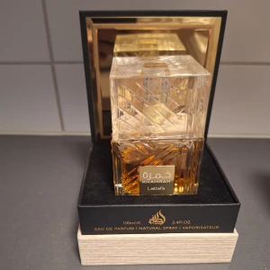 Lattafa Khamrah Eau de Parfum 100ml - Lattafa Khamrah är en lyxig parfym i en kristallmönstrad, fyrkantig glasflaska med guldiga detaljer. Doften har söta, varma och kryddiga toner av vanilj, amber, kanel och trä, med inslag av frukt och fräschör. Flaskan rymmer 100 ml och utstrålar exklusivitet. (Ni ser mängd kvar)