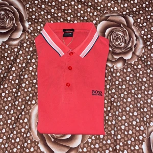 Rosa pikétröja från Hugo Boss - Rosa pikétröja från Hugo Boss med klassisk krage och knäppning framtill. Köpt från auktoriserad butik, Hanzens, Umeå