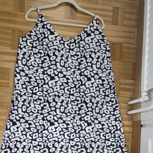 Svartvit långklänning med mönster - Snygg långklänning med smala axelband och v-ringning. Klänningen har ett svartvitt abstrakt mönster som verkligen sticker ut. Perfekt för dig som gillar att synas och vill ha något unikt i garderoben.