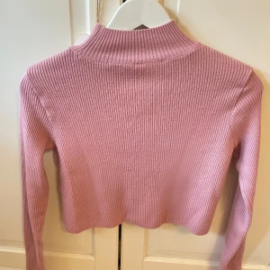 Rosa ribbad croppad polotröja - Säljer en söt rosa ribbad polotröja med croppad passform. Tröjan har lång ärm och hög hals. Normal i storleken, passar alla i storlek mellan XS-M.