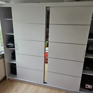 Vit garderob  - Bilderna visar en stor vit garderob med skjutdörrar och flera hyllor fyllda med kläder. Ingen bok syns på bilderna. Man kan ej hitta samma garderob för 4000 alla andra kostar 10-15 tusen för mindre pris kontakta 0763181323