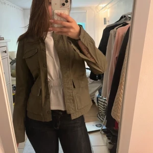 Olivgrön jeansjacka - Snygg olivgrön jeansjacka med fyra stora fickor framtill och klassisk krage. Jackan har knäppning med knappar och perfekt för lager-på-lager. Passformen är normal och jackan är långärmad – en riktig garderobsklassiker. (Två första bilderna är lånade)  Hör av dig vid frågor.☺️