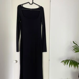 Svart långärmad maxiklänning - En stilren svart långklänning med lång ärm och fyrkantig urringning. Klänningen formar sig väldigt fint på kroppen. Säljer då den inte kommer till användning, den är använd max 2 gånger. Klänningen har ett glansigt material. Återkom gärna vid fler bilder på hur klänningen sitter på.