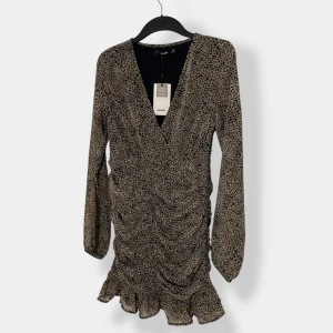 Leopardmönstrad kortklänning Bik Bok - Kort klänning från Bik Bok i leopardmönster med v-ringning, långa ärmar och volangkant nertill. Klänningen har rynkade detaljer framtill och är tillverkad i återvunnen polyester. Perfekt för dig som vill sticka ut med en trendig look.