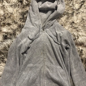 Grå hoodie från Juicy Couture XXS - !!Kan köpas med byxorna, få 400kr rabatt om man köper dem som par!!Grå zip-hoodie från Juicy Couture i storlek XXS. Klassisk modell med huva, snörning och fickor framtill. Broderad JC-logga på bröstet och snygga metalldetaljer på snörena. 