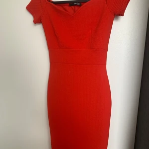 Röd kortklänning från Two Two - Snygg röd kortklänning med v-ringning och markerad midja. Klänningen har korta ärmar och en figurnära passform. Materialet är strukturerat och dragkedja finns i ryggen. Perfekt för dig som vill sticka ut med en klassisk och stilren look.