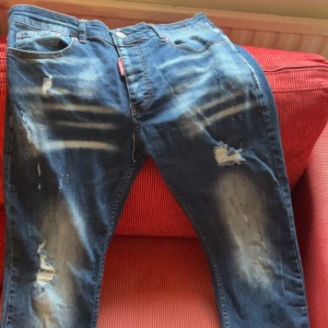 Dsquared2 slitna blå jeans - Riktigt snygga blå jeans från Dsquared2 med slitningar och trasiga detaljer framtill. Jeansen har klassisk femficksmodell, normal passform och cool tvätt med ljusa partier. Perfekta för dig som gillar en edgy streetstil.