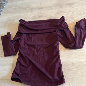 Vinröd offshoulder topp Gina Tricot - Säljer en vinröd offshoulder topp från Gina Tricot i mjuk bomull. Toppen har långa ärmar och en bred, vikt krage som ger en snygg och trendig look. Perfekt för dig som vill sticka ut med en stilren och modern vibe.