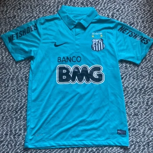 Santos Neymar Jr  - HELT NY! Säljer en blå Santos fotbollströja från Nike med Neymar Jr och nummer 11 på ryggen. Tröjan har korta ärmar, krage och tryckta sponsorer som BMG och Netshoes. Perfekt för dig som gillar brasiliansk fotboll och vill sticka ut på planen.