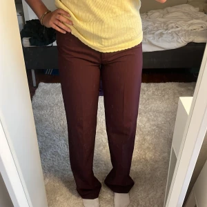 Vinröda kostymbyxor från Vero Moda - Vinröda kostymbyxor från Vero Moda i rak modell. Byxorna har medelhög midja och stängs med dragkedja och ett litet metallspänne fram. Materialet är mjukt och svalt. Byxan är både bekväma och mycket stilren. Perfekta att matcha med en enkel topp eller skjorta. 😍 Säljer då de är lite för tajta vid rumpan. Brukar bara 36, och då dessa är 36 skulle jag nog säga att de också passar 34! Aldrig använda, fått från min mamma så det är från de gamla sortimentet från Vera Moda🔥Priset motsvarar kvaliteten💫