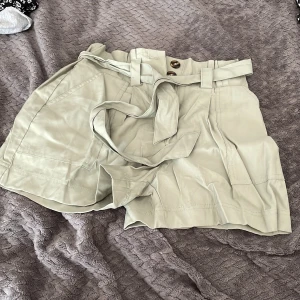 Gröna shorts med knytbälte - Snygga ljus gröna shorts med hög midja och brett knytbälte i midjan. De har stora fickor framtill, papperspåse-midja och stängs med knappar. Perfekta för en chill och trendig look under varma dagar.