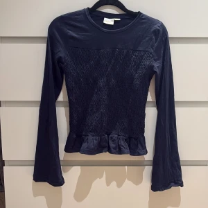 Mörkblå långärmad topp Gina Tricot - Supersöt mörkblå långärmad topp från Gina Tricot, är smockad i midjan och volangkant nedtill. Använd 2 gånger ❤️