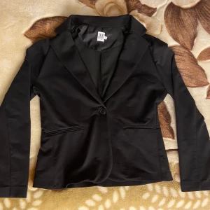 Saint Tropez damkavaj i stl M - Stilren och figursydd svart damkavaj från Saint Tropez i storlek M. Klassisk modell med en knapp framtill och två fuskfickor. Tunn och mjuk i materialet – bekväm att bära både till vardags och vid festligare tillfällen. Passar lika bra över en klänning som till jeans. Använd fåtal gånger, inga tecken på slitage.   Modell: P4036 Material: 75% bomull, 21% polyester, 4% elastan Kall maskintvätt i 30 grader.  Nypris: 699 kr 