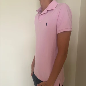 Ralph Lauren pike - Säljer en rosa pikétröja från Polo Ralph Lauren i modellen Custom Slim Fit. Klassisk krage, korta ärmar och broderad logga på bröstet. Tillverkad i mjuk bomull som känns skön mot huden. Perfekt för en clean och stilren look. Denna modellen är sjukt sällsynt också. Nypris 1499. 