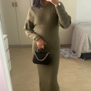 Olivgrön ribbad långklänning - Snygg olivgrön långklänning i ribbstickat material med lång ärm och rund hals. Klänningen har en figurnära passform och är perfekt för dig som gillar en stilren och enkel look. Passar lika bra med sneakers som boots.