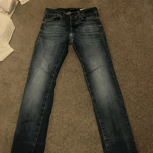 Blå jeans 27/30 med slim fit - Säljer ett par blå jeans i klassisk straight fit med snyggt slitna detaljer och femficksmodell. Jeansen har normal passform och är tillverkade i jeansmaterial. Perfekta för dig som gillar en tidlös look.
