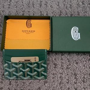 Grön plånbok med snygga mönster - Snygg grön plånbok med mönster i vitt och brunt. Plånboken är tillverkad i skinn och har flera kortfack. Kommer i originalask med gul putsduk. Perfekt för dig som vill ha något exklusivt och stilrent i fickan. Helt ny aldrig använd.