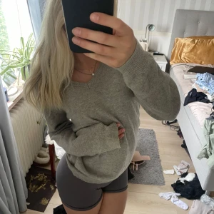 Grå v-ringad stickad tröja - Mysig grå stickad tröja med v-ringning och långa ärmar. Den har ribbade muddar vid ärmslut och nederkant. Enkel att matcha med både jeans och tights. Storlek XS.