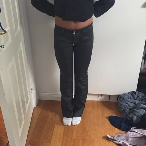 Svarta bootcut skinn byxor från Nelly  - Säljer ett par svarta byxor med bootcut och snygga fickdetaljer framtill. Byxorna har låg midja, dubbla knappar och är gjorda i ett glansigt material som ger en cool look. Perfekta om du vill sticka ut lite extra.