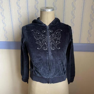 Svart velour hoodie med fjäril - Svart velour hoodie med dragkedja och huva. Framsidan har en fjäril i silvriga nitar. Barnstorlek men passar s, eventuellt m. 🩷