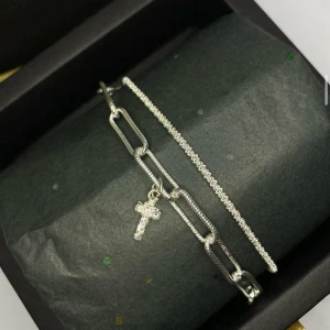 Silverarmband med kors och kedjelänk - Två stilrena silverarmband, ett med glittrande korsberlock och stora kedjelänkar, det andra med tunn, glittrig kedja. Ej använd utan kommer från min small business.
