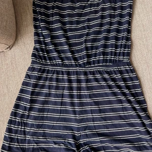 Randig marinblå playsuit från Gina Tricot - Snygg marinblå playsuit från Gina Tricot i storlek L. Den har vita horisontella ränder och resår i midjan för en bekväm passform. Tillverkad i mjuk bomull och polyester, perfekt för en avslappnad och marin look.