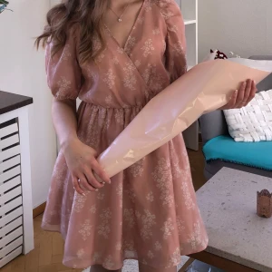 Rosa blommig omlottklänning H&M - Supersöt kort rosa klänning från H&M med vitt blommönster. Omlottmodell med v-ringning, puffiga korta ärmar och knyt i midjan. Lätt och flowy känsla, perfekt för vår och sommar. Materialet är mjukt och skönt mot huden.