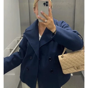 Design by si kappa - Super snygg mörkblå kappa med dubbelknäppning och bred krage. Jackan har långa ärmar med knappar vid ärmslut och en rak, loose passform. Perfekt för dig som vill ha en klassisk och stilren look. Materialet är ull som håller dig varm under kyliga dagar. 