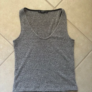 Ribbad grå linnetopp från Mango - Säljer en ribbad grå linnetopp från Mango Basics. Toppen är ärmlös med djup v-ringning och har en snygg, stickad struktur. Perfekt att matcha med jeans eller kjol för en chill och stilren look.
