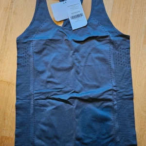  träningstopp XL - Säljer en mörkgrå seamless träningstopp från Fabletics i storlek XL. Toppen har brottarrygg, ventilerande perforerade detaljer och är tillverkad i stretchigt material som andas. Perfekt för dig som vill ha en smidig och bekväm topp till gymmet eller löprundan.