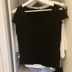 Svart topp från att. med kort ärm - En stilren svart topp från att. med rund halsringning och korta ärmar. Enkel och clean design som passar till många olika looks. Tunt och mjukt material som känns skönt mot huden. Perfekt att matcha med jeans eller kjol för en snygg outfit.