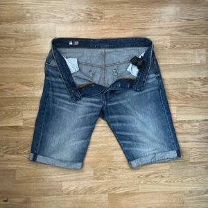 G-Star RAW 3301 Shorts- perfekt sommarstil! Stl 31 (M) - G-Star RAW 3301 Shorts - Perfekt sommarstil! Stl 31 (M) Säljer ett par G-Star RAW 3301 shorts i storlek 31, vilket motsvarar Medium (M). Dessa shorts är tillverkade i högkvalitativ denim med en snygg, blekt tvätt som ger dem en vintage-känsla. De har flera praktiska fickor och stängs med både knapp och dragkedja. Perfekta för en avslappnad och trendig look i sommar!  *   Märke: G-Star RAW *   Modell: 3301 *   Storlek: 31 (M) *   Material: Denim *   Skick: Bra, använda men väl omhändertagna *   D