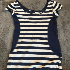 Randig kortklänning från Gina Tricot - Superfin kortklänning från Gina Tricot i marinblått och vitt med klassiskt horisontellt randigt mönster. Klänningen har rund halsringning och korta ärmar. Perfekt för en avslappnad och stilren look.