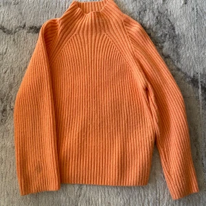 Ribbad orange stickad tröja Gina Tricot - Superfin ribbstickad tröja från Gina Tricot i en härlig orange färg. Tröjan har hög hals och långa ärmar, perfekt för att hålla värmen. Den är mjuk och skön, med en loose fit som ger en chill vibe. Passar perfekt till jeans eller kjol.