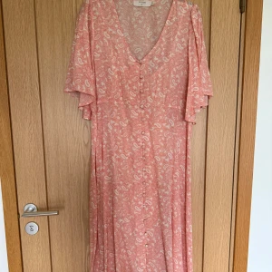 Paisleymönstrad långklänning från Cream - Långklänning från Cream med paisleymönster, v-ringning och knappar framtill. Klänningen har korta, vida ärmar och ett luftigt fall. Tillhörande underklänning. Perfekt för sommarens alla tillfällen.