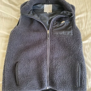 Mörkblå fleeceväst från lager 157 - Mysig mörkblå fleeceväst från 157 med hög krage och hel dragkedja framtill. Västen har två sidofickor och en bröstficka med dragkedja. Perfekt för lager-på-lager och chill dagar. Fodrad insida för extra komfort.