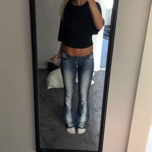 Blå bootcut jeans med slitningar - Säljer ett par blå bootcut jeans med ljusa tvättade partier. Jeansen är lågmidjade och sköna 