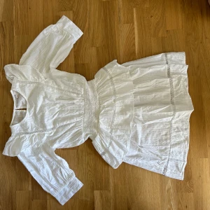 Vit kortklänning från Name It - Superfin vit kortklänning från Name It med volangdetaljer och smock i midjan. Klänningen har trekvartsärm och är tillverkad i ett lätt bomullstyg med diskret struktur. Perfekt för sommarens alla tillfällen!