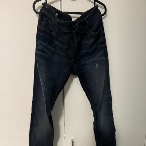 Mörkblå jeans från Jack & Jones - Säljer ett par mörkblå herr jeans från Jack & Jones med snygga slitningar och kontraster. Storlek 34/S. 