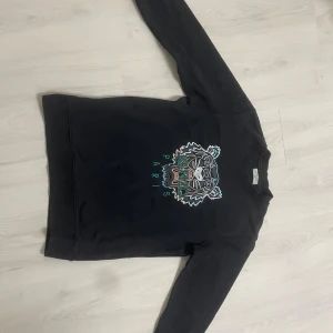 Svart Kenzo sweatshirt med tigertryck - Svart sweatshirt från Kenzo med ikoniskt broderat tigerhuvud och texten 'KENZO PARIS' framtill i grönt och vitt. Tröjan är använd ca 7 gånger. Priset kan diskuteras 