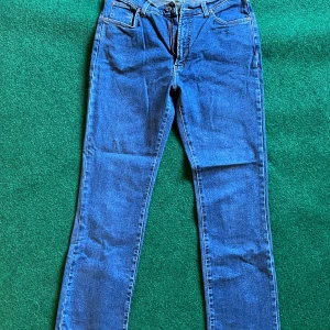 Blå jeansbyxor från KappAhl, extra långa - Snygga blå jeansbyxor från KappAhl i extra lång modell. Klassisk femficksdesign med dragkedjegylf och raka ben. Tillverkade i stretchigt material med 96% bomull och 4% elastan för skön passform.