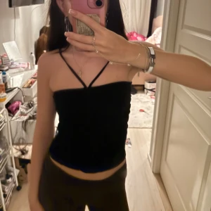 Svart croppad linnetopp med smala band - Säljer en svart croppad linnetopp med tunna axelband och snygg detalj framtill där banden korsas. Toppen har en enkel och stilren look som passar perfekt till jeans eller kjol. Mjuk och skön mot huden, perfekt för varma dagar.