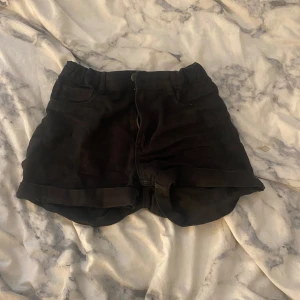Svarta shorts från H&M, strl 152 - Svarta shorts från H&M med klassisk femficksdesign och uppvikta benslut. De har normal passform och stängs med dragkedja och knapp. Perfekta för sommaren och enkla att matcha med allt. Materialet är mjukt och bekvämt, troligtvis bomull.