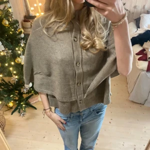 Beige stickad poncho med knappar - Supermysig beige stickad kofta med bred passform och snygga träknappar framtill. Lapparna är bortklippta då jag tyckte de kliade. Nypris:699