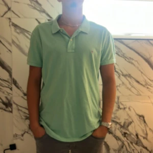 Mintgrön pikétröja från GANT - Snygg mintgrön pikétröja från GANT i slim fit-modell. Klassisk krage, korta ärmar och knappar framtill. Broderad GANT-logga på bröstet. Perfekt för en fräsch och stilren look under varmare dagar.