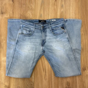 Replay Anbass ljusblå jeans 30/32 - Snygga ljusblå Replay Anbass jeans med klassisk femficksdesign och diskreta slitningar. Jeansen har raka ben och normal passform, tillverkade i mjuk bomullsdenim med lite stretch för extra komfort. Perfekta för en avslappnad och trendig look.