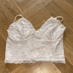 Vit spetsig linnetopp från BikBok - Supersöt vit linnetopp från BikBok i spets med blommigt mönster och tunna axelband. Toppen har v-ringning, stretchig rygg och fina spetsdetaljer längs kanterna. Perfekt att styla med jeans eller kjol för en fräsch look.